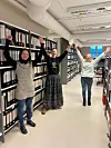 Tre personer står mellom bokhyller i et bibliotek med armene løftet.