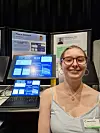 Nora Storrø smiler ved en stand med laptop og skjermer som viser grafer og digitalt verktøy.