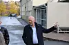 En mann gestikulerer utenfor en større bygning, mens to personer står delvis synlig i forgrunnen.